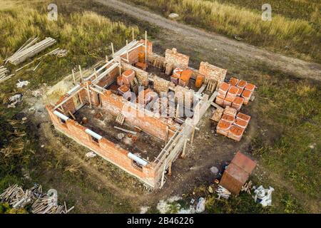 Luftbild der Baustelle für zukünftiges Ziegelhaus, Betonfundament und Stapel gelber Lehmziegel für den Bau. Stockfoto