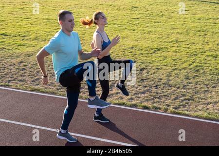 Junges Paar von fit Sportler Junge und Mädchen laufen, während sie Übung auf den roten Titel der öffentlichen Stadion im Freien. Stockfoto