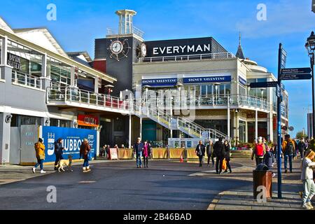 Die Menschen schlendern im Winter unter der Sonne unter den vielen Bars, Geschäften und Restaurants im Mermaid Quay in Cardiff Bay. Die Gegend ist bekannt als "Tacoma-Platz". Stockfoto