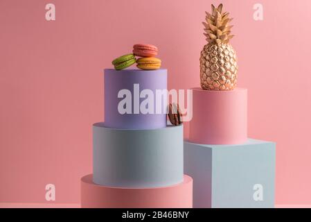 Verschiedene bunte Makronen und goldene Ananas auf pinkfarbenem Hintergrund Stockfoto