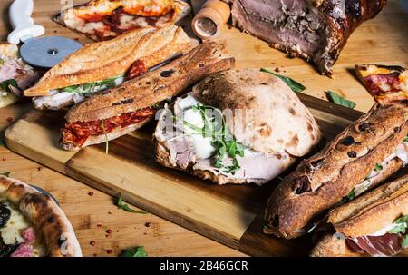 Flache, geschlossene Auswahl an Sandwiches und Pizza auf Holzschneidebrett. Mediterrane Küche Stockfoto