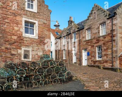 Hummertöpfe, die von alten Steinhäuschen auf einer gepflasterten Straße am Hafen in Crail East Neuk von Fife Scotland gestapelt sind Stockfoto