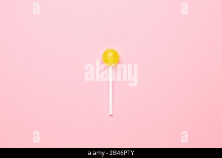 Süßlicher gelber Lolipop auf pastellrosa Hintergrund. Minimalistische Komposition Draufsicht. Stockfoto