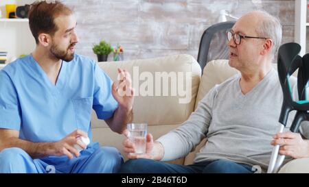 Männliche Krankenschwester, die dem pensionierten Mann im Pflegeheim Pillen gibt. Stockfoto