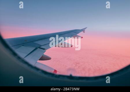Ansicht aus dem Flugzeugfenster. Flügel während des Flugs über Wolken bei schönem Sonnenuntergang. Stockfoto