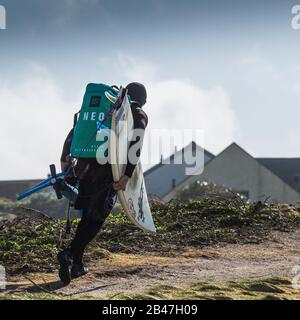 Ein Kite-Boarder, der seine Ausrüstung mit sich führt und mit dem Mühe kämpft, in Fistral in Newquay in Cornwall in sehr starke Winde zu gehen. Stockfoto