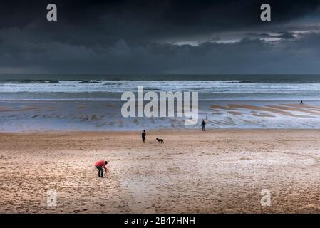 Hundegänger und ihre Haustiere am Fistral Beach, während dunkle Regenwolken Newquay in Cornwall nähern. Stockfoto