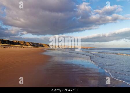 Ein leerer Strand von St Cyrus, der nach Norden blickt, mit den Sea Cliffs und der Landspitze, die von der Einstellung "February Sun" angezündet werden. Stockfoto