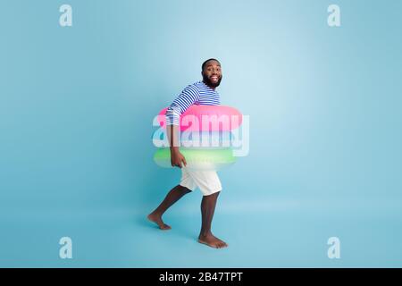 Großes Profil Seitenfoto positiv afro amerikanischer Kerl Tourist Urlaub gehen barfuß schwimmen Ozean halten bunte Lebensretter tragen gestreifte Weste Stockfoto