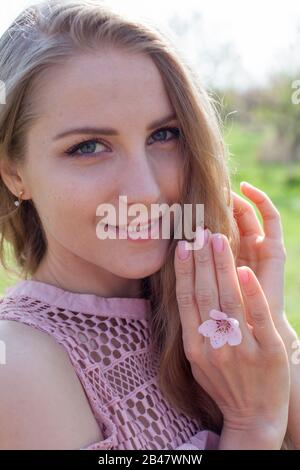 Schöne blonde Frau in rosafarbenem Kleid und Marienkleid an der Hand Stockfoto