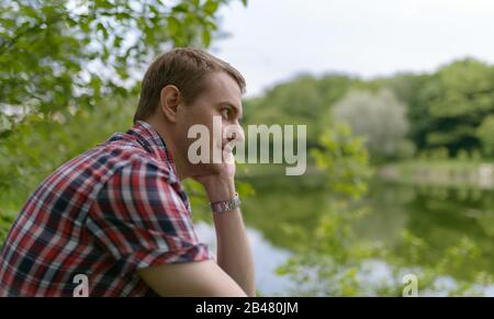 Der junge pensive Mann blickt auf den Fluss. Einheit mit der Natur. Stockfoto