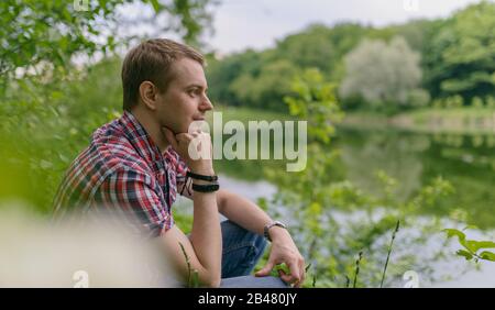 Der junge pensive Mann blickt auf den Fluss. Einheit mit der Natur. Stockfoto