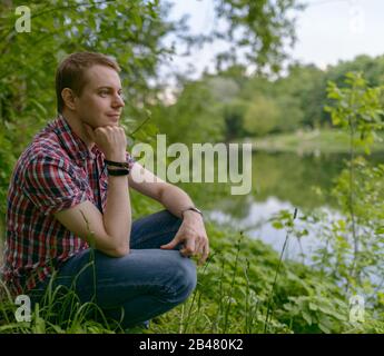 Der junge pensive Mann blickt auf den Fluss. Einheit mit der Natur. Stockfoto