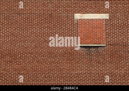 Ein einzelnes Fenster oben auf einer roten Ziegelwerkwand in einer Ferne Stockfoto