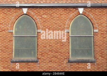 Ein Paar retro gewölbte alte Kirchenfenster an einer roten Ziegelwand Stockfoto