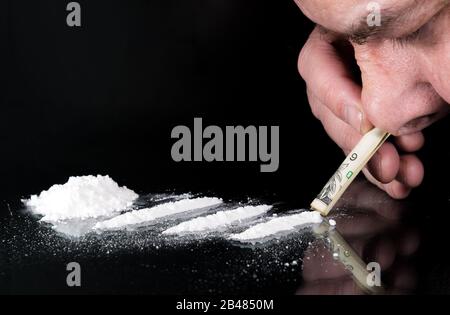 Schnarchen einer Linie von Kokain. Auf einem Glastisch befinden sich drei Linien, auf der linken Seite ein Stapel. Die Nase einer Person schnorchelt durch einen gerollten Schein. Stockfoto