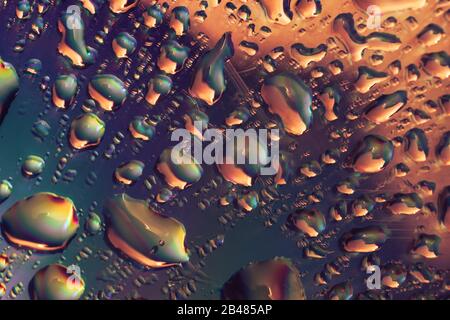 Nahaufnahme schöner Wassertropfen mit grünem, rotem und orangefarbenem Licht in holografischem Effekt. Hintergrundmuster für das Design. Makrofotografie VI Stockfoto