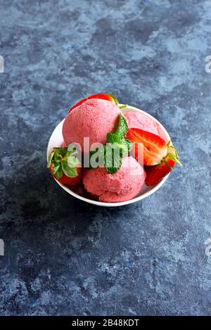 Erdbeer-Eisschaufel mit frischen Erdbeeren in der Schüssel über blauem Steingrund mit freiem Text. Leckeres kaltes Sommerdessert. Stockfoto