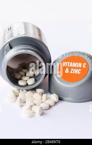 Pillen, die aus einer Flasche Vitamin C und Zink-Ergänzungstabletten zur Stärkung des Immunsystems verschüttet werden Stockfoto