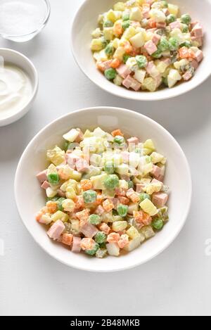 Olivier Salat aus gekochtem Gemüse und Wurst mit Mayonnaise in Schüssel. Russisches Neujahr oder Weihnachtssalat auf weißem Steingrund. Nahansicht Stockfoto