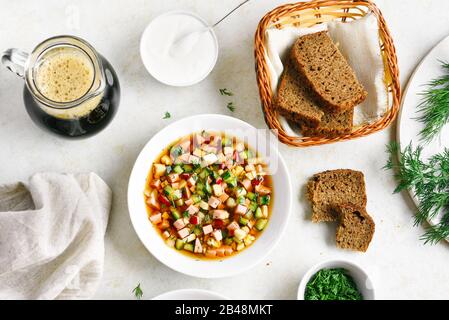 Leckere kalte russische Suppe Okroschka mit Wurst, Gemüse und Kvass über hellem Steingrund. Draufsicht, flacher Lay Stockfoto