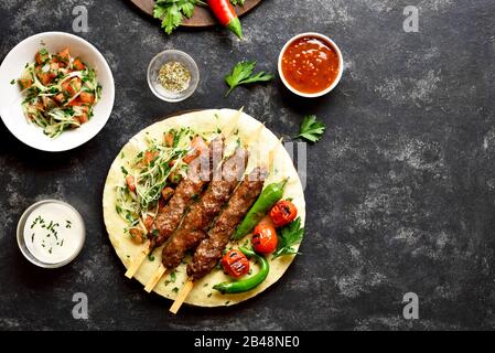 Türkische Adana Kebab mit frischem Gemüse auf Fladenbrot über schwarzem Steinhintergrund mit freiem Textbereich. Draufsicht, flacher Lay Stockfoto