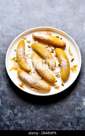 Frittierte Bananen auf weißem Teller über blauem Steinhintergrund mit freiem Textbereich. Leckeres Dessert aus panfrittierten Bananen im asiatischen Stil. Stockfoto