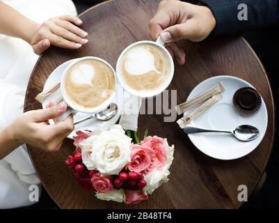 Hände von Braut und Bräutigam mit Latte Art Kaffeetasse. Ehekonzept Stockfoto