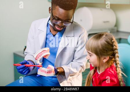 Junges schönes Mädchen im Zahnarztbüro. Der afrikanische Kinderzahnarzt untersucht die Zähne eines Kindes Stockfoto