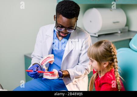 Junges schönes Mädchen im Zahnarztbüro. Der afrikanische Kinderzahnarzt untersucht die Zähne eines Kindes Stockfoto