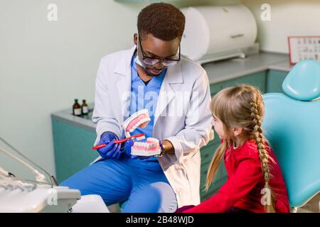 Junges schönes Mädchen im Zahnarztbüro. Der afrikanische Kinderzahnarzt untersucht die Zähne eines Kindes Stockfoto