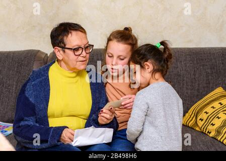 Oma, Die Alte Fotos Mit Enkeln Betrachtet, Um Die Erinnerung Zu Aktualisieren. Glückliche Familie, Gemütliche Heimmomente. Stockfoto