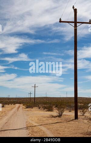 Die Straße in der Wüste ist schmutzig, mit Pfosten, die die Seite der Straße unter einem wundervollen, sommerlichen blauen Himmel mit Wolken sägen Stockfoto