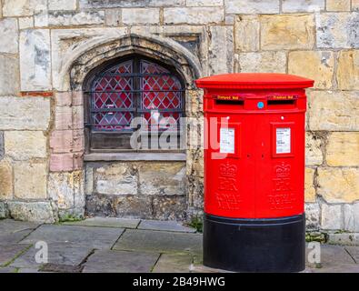 Traditioneller roter Postkasten in York mit steinernem Wandhintergrund Stockfoto