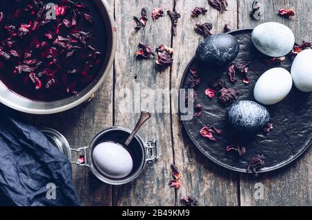 Gefärbte Ostereier mit Marmorsteineffekt, bemalt mit Naturfarbstoff Karkattee aus Hibiskusblüten auf altem Holzhintergrund. Färbevorgang von Eiern Stockfoto