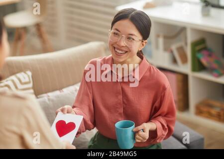 Horizontales Hochwinkel-Überschulterporträt der glücklichen asiatischen Frau, die von ihrer Tochter eine Tagestarte für handgefertigte Mütter erhält Stockfoto