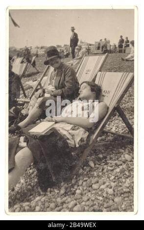 Anfang der 1920er Jahre ein offenes Foto von Frauen in Liegestühlen, die eine schläft, die andere lacht über ihre Freundin. Auf der Rückseite der Postkarte steht „August 1928, Brighton“ Brighton, Sussex, England, UK Retro Beach Photo Stockfoto
