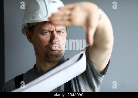 Mann, der einen harten Hut trägt, hält sich in den Händen Blaupause kontrolliert die Baustelle Stockfoto