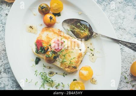 Frittierter salziger Fetakäse, in Brotkrümel mit aufgepepptem Thymianhonig und farbenfroher Tomatenkirsche bestrichen. Vegetarisches Konzept für gesundes Essen. Draufsicht. Stockfoto