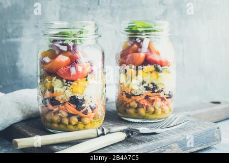 Köstlicher frischer vegetarischer bunter Salat in den Gläsern mit Kichererbsen, Paprika, Gurke, Karotte, getrockneten Preiselbeeren, Tomaten, roter Zwiebel und Kürbisse Stockfoto