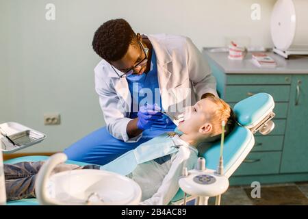 Kinderzahnheilkunde, pädiatrische Zahnheilkunde. Ein männlicher afroamerikanischer Stomatologe behandelt Zähne eines Jungen im Schulalter. Mundgesundheit und Hygiene. Stockfoto