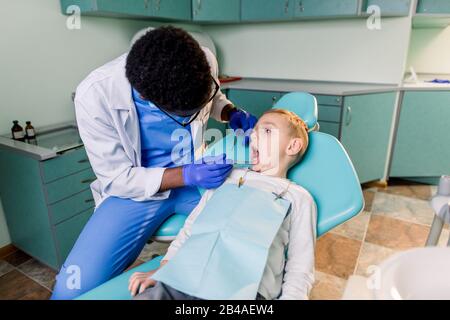 Junger schöner Junge im Zahnarztbüro. Der afroamerikanische Kinderzahnarzt untersucht die Zähne eines Kindes Stockfoto