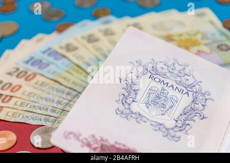 Rumänisches Konzept. Der rumänische Pass und die rumänischen Banknoten/Münzen auf blauem und rotem Hintergrund. Kolosseup des rumänischen Passes und der rumänischen Währung Stockfoto