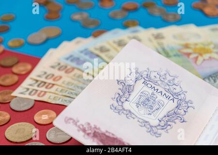 Rumänisches Konzept. Der rumänische Pass und die rumänischen Banknoten/Münzen auf blauem und rotem Hintergrund. Kolosseup des rumänischen Passes und der rumänischen Währung Stockfoto