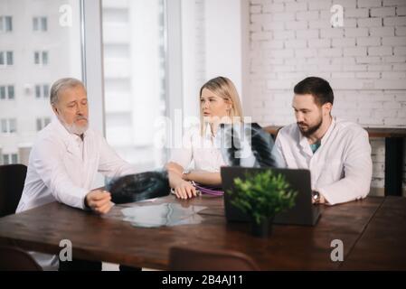 Leitender männlicher Arzt und junger bärtiger Arzt, der das Röntgenbild analysiert Stockfoto