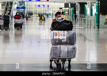 Hongkong, China. März 2020. Reisende, die eine Gesichtsmaske als Vorsichtsmaßnahme gegen den Ausbruch von Coronavirus tragen, drängen einen Wagen am internationalen Flughafen Hongkong.Da sich das Coronavirus (Covid-19) weiterhin auf der ganzen Welt ausbreitet, haben viele Länder die Reisebeschränkungen verschärft. Credit: Sopa Images Limited/Alamy Live News Stockfoto