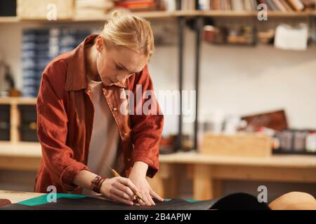 Hotizontaler Mittelschuss der konzentrierten jungen Frau, die am Tisch steht und in der modernen Handwerkerwerkstatt arbeitet Stockfoto