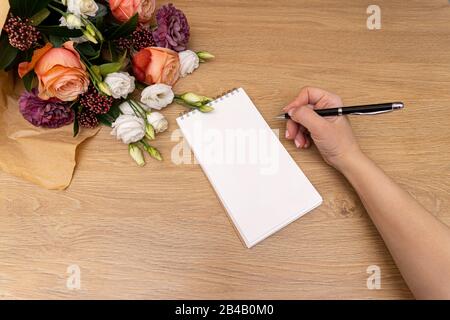 Blumenstrauß aus Rosen auf Holzhintergrund, Notizbuch und Bleistift in Frauenhand. Stockfoto