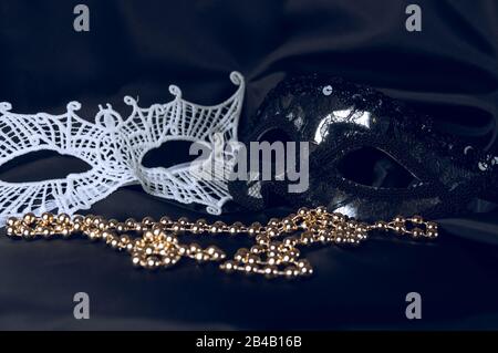 Weiße und schwarze Karnevalsmasken und Perlen auf schwarzem Hintergrund. Accessoire für Karneval. Stockfoto