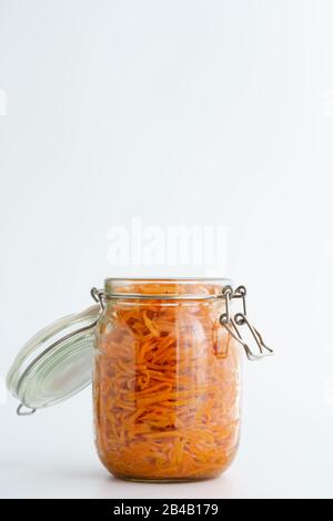 500 Gramm würziger koreanischer Karottensalat mit Öl, Knoblauch und schwarzem Pfeffer im Glasbecher. Nachhaltige Verpackung, weißer Hintergrund, hohe Auflösung Stockfoto